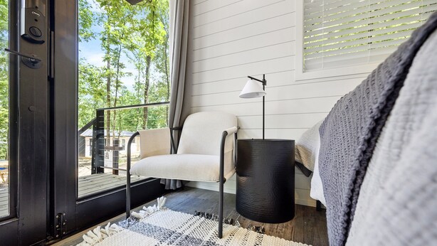 Una habitación moderna con un ventanal grande, una silla blanca, una lámpara de pie negra y una alfombra con textura.