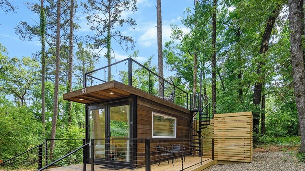 A wooden cabin with a glass door, a deck, and a spiral staircase.
