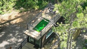 A modern cabin with a deck, a small pool, and a view of the surrounding forest.