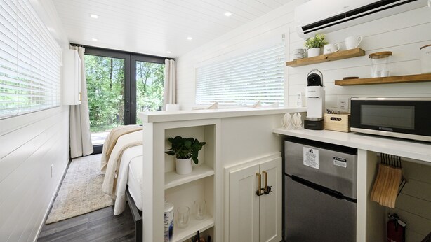 A modern kitchen with white cabinetry, a built-in microwave, and a refrigerator. There are wooden shelves above the counter holding kitchen items.