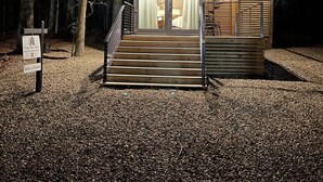 A cabin with a wooden deck and a glass door entrance, surrounded by trees.