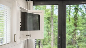 A modern interior with a mounted television, white walls, and a door leading to an outdoor area with trees.