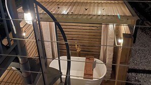A small, enclosed wooden cabin with a sloped roof, a bathtub, and a window.