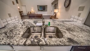 Une cuisine dotée d’un plan de travail en granit, d’un évier double et d’un coin repas avec un banc et une table.