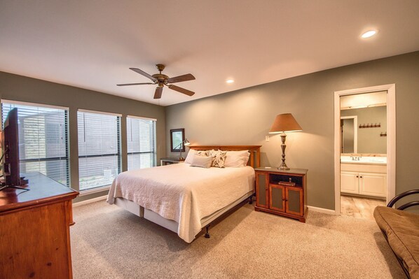 A bedroom with a bed, a nightstand, a lamp, a ceiling fan, and a bathroom with a mirror and sink.