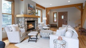 A cozy living room with a stone fireplace, wooden beams, and a large window. - 405 Greenway Circle 4 Bedroom Home by RedAwning (Avon)
