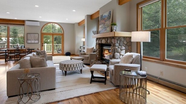 A spacious living room with a stone fireplace, comfortable seating, and large windows offering a view of the outdoors. - 405 Greenway Circle 4 Bedroom Home by RedAwning (Avon)