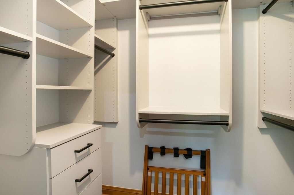 A white closet with shelves, a hanging rod, and a wooden chair.