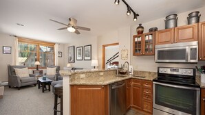 A kitchen with wooden cabinets, a stainless steel oven, and a microwave. There is a dining area with a table and chairs. - Value Unit 1422 - 2br - Zephyr Mountain Lodge 2 Bedroom Condo (Winter Park)