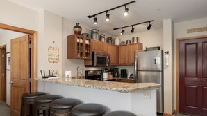 A kitchen with wooden cabinets, granite countertops, stainless steel appliances, and bar stools. - Value Unit 1422 - 2br - Zephyr Mountain Lodge 2 Bedroom Condo (Winter Park)