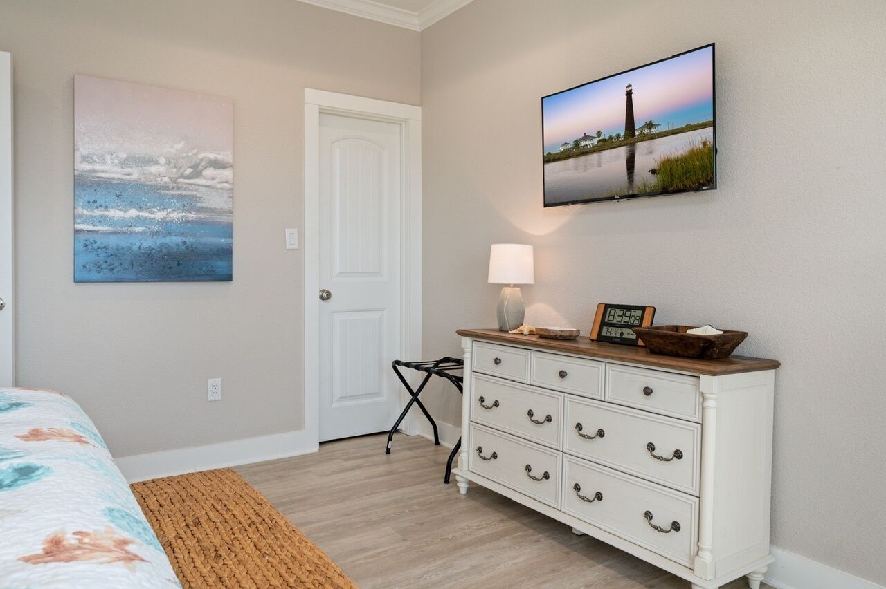 A bedroom with a bed, a dresser, a lamp, and two paintings.