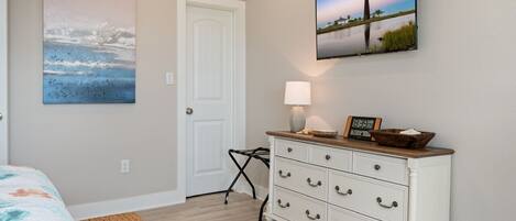 A bedroom with a bed, a dresser, a lamp, and two paintings.