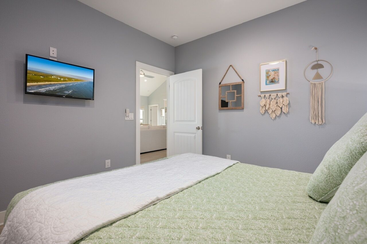 A bedroom with a bed, a television on the wall, a door leading to another room, and wall decorations.