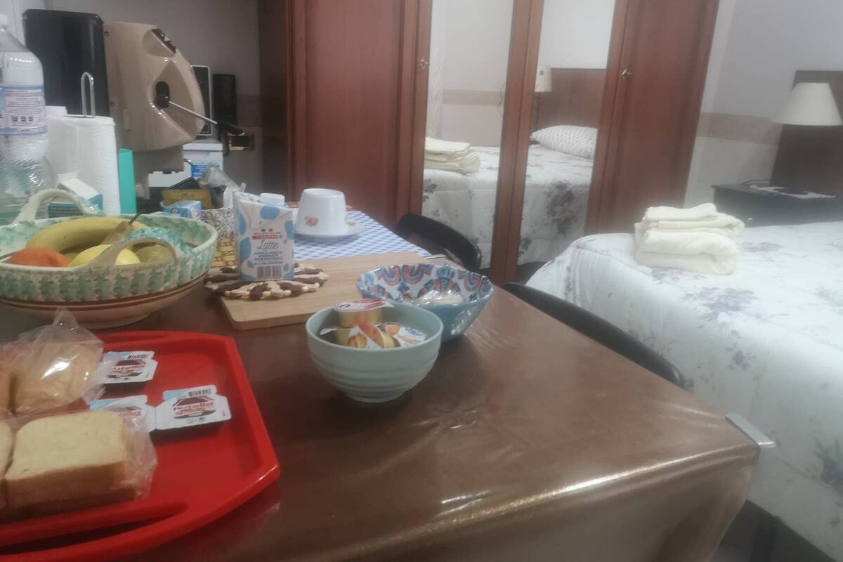 Une chambre d’hôtel avec une table à manger dressée, un lit recouvert d’une courtepointe à motifs floraux, et une vue sur une autre chambre à travers une porte.
