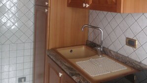 A kitchen with wooden cabinets, a sink, and a tiled backsplash. - Antico Portale Host Roberto (Regalbuto)