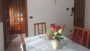 A dining area with a table set for two, a vase with flowers, and a wooden door with glass panels. - Antico Portale Host Roberto (Regalbuto)