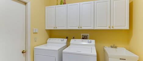 A laundry room with two front-loading washers and a stacked dryer, white cabinetry above, and a white sink.