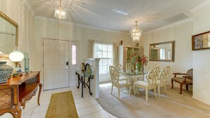 Uma sala de jantar com mesa de vidro, cadeiras brancas, aparador de madeira e lustre.