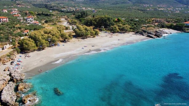 Un pueblo costero con una playa de arena, aguas turquesas cristalinas y edificios dispersos.