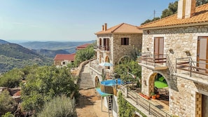 A stone building with a red-tiled roof, a balcony, and a view of the surrounding landscape.