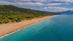 Un paysage côtier avec une plage, des eaux turquoise et limpides, et des collines verdoyantes en arrière-plan.