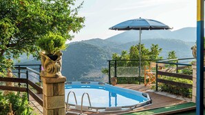 Une piscine avec vue sur les montagnes, entourée d’une terrasse en bois et d’un pilier en pierre.