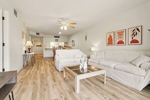 Ein modernes Wohnzimmer mit Holzboden, weißen Sofas, einem Couchtisch und einem Deckenventilator.