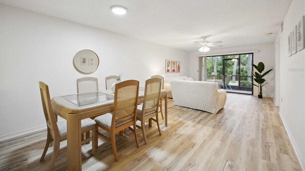 A modern dining area with a glass table and wooden chairs, a ceiling fan, and a view of the outdoors through a sliding glass door. - 2 Bed 2 Bath Condo on Golf Course in Quiet Safe Community, 4 Miles to Beach (Venice)