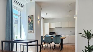 Eine moderne Küche mit weißen Schränken, einer Mikrowelle und einem Spülbecken. Ein Essbereich mit Tisch und Stühlen sowie ein Blumentopf sind ebenfalls vorhanden.