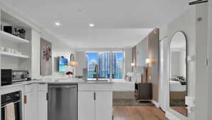 Une cuisine moderne avec des meubles blancs, un lave-vaisselle, un four à micro-ondes et une cuisinière. Une grande fenêtre offre une vue sur le paysage urbain.