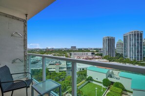 Ein Balkon mit Glastisch und Stuhl mit Blick auf eine Stadtlandschaft aus modernen Gebäuden und einem grünen Park.