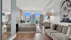 Une chambre d’hôtel moderne dotée d’un grand lit, d’un canapé, d’un bureau et offrant une vue sur le paysage urbain.