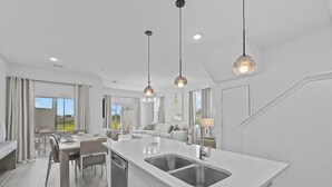 Une cuisine moderne dotée d’un îlot central, d’appareils électroménagers en acier inoxydable et de luminaires suspendus.