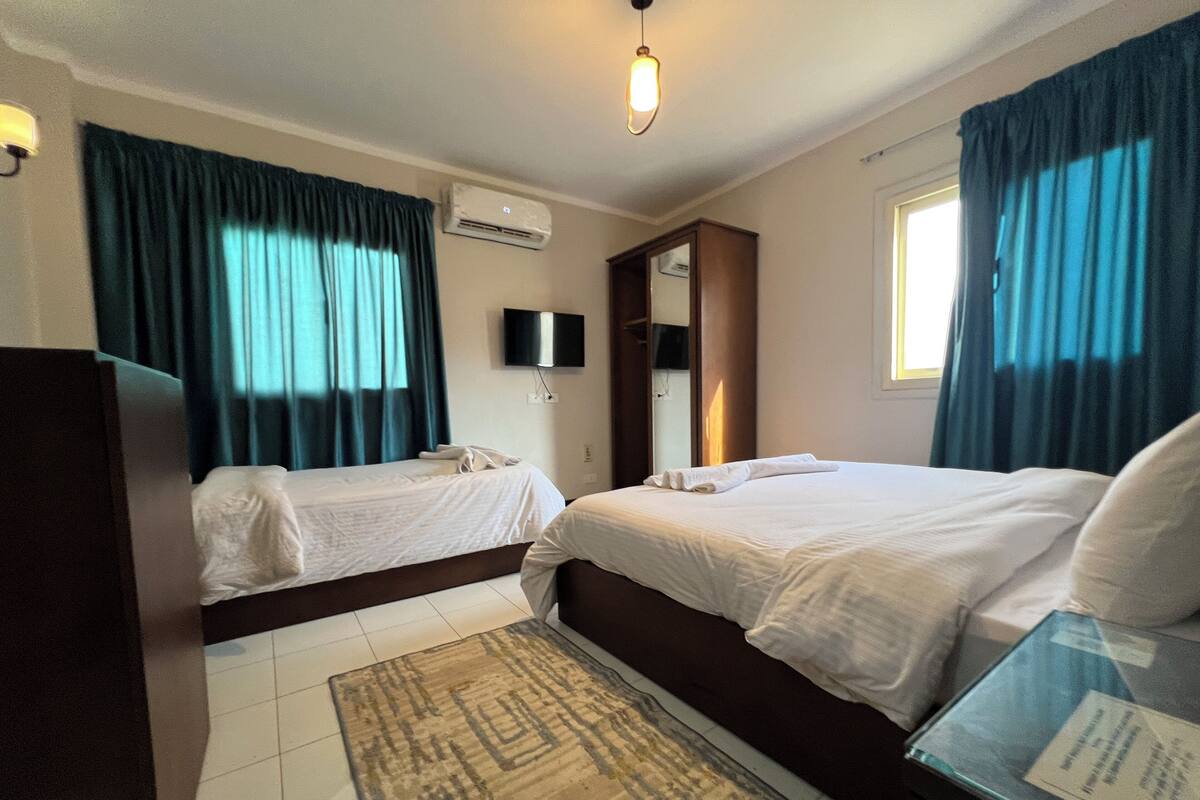 A hotel room with two beds, a flat-screen TV, an air conditioning unit, and a small rug.