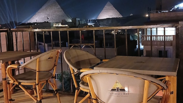 Un espace extérieur aménagé avec des chaises et une table en bambou, offrant une vue sur les pyramides en arrière-plan.