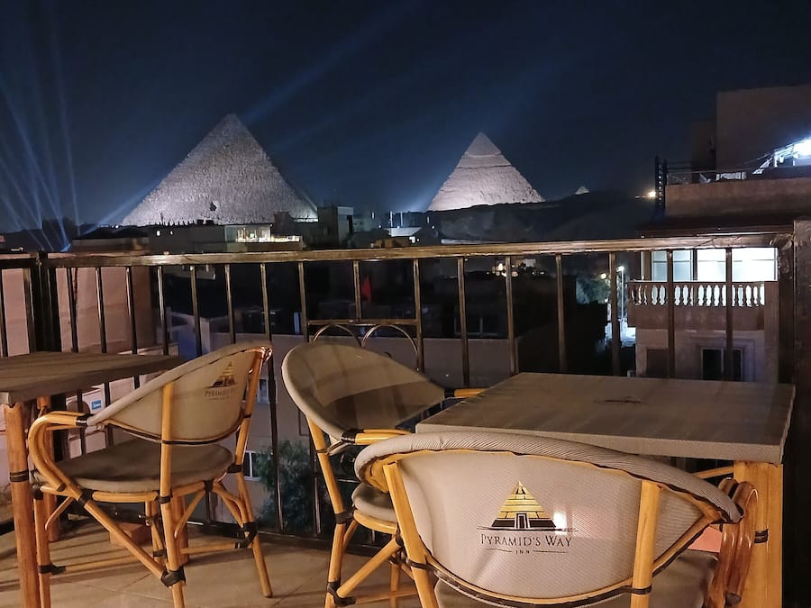Un espacio al aire libre con sillas de bambú y una mesa, con vistas a pirámides al fondo.