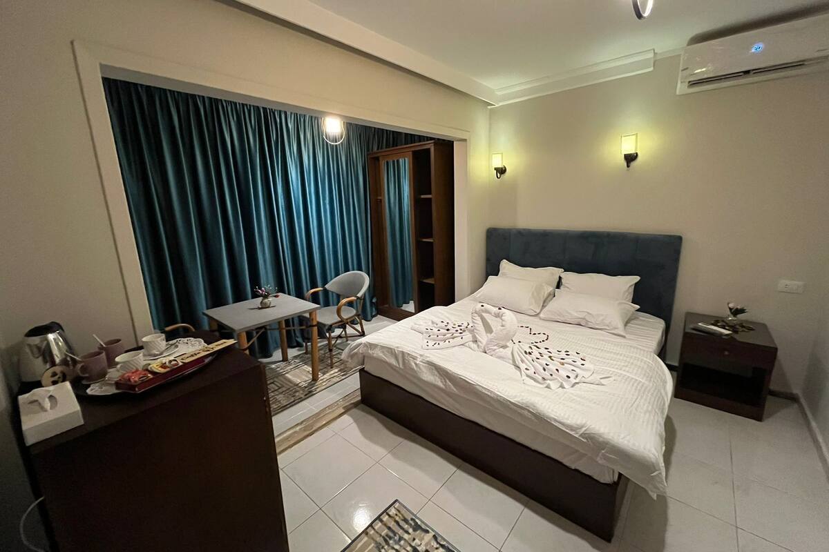 A hotel room with a bed, a desk, a chair, a small table, and a wardrobe.