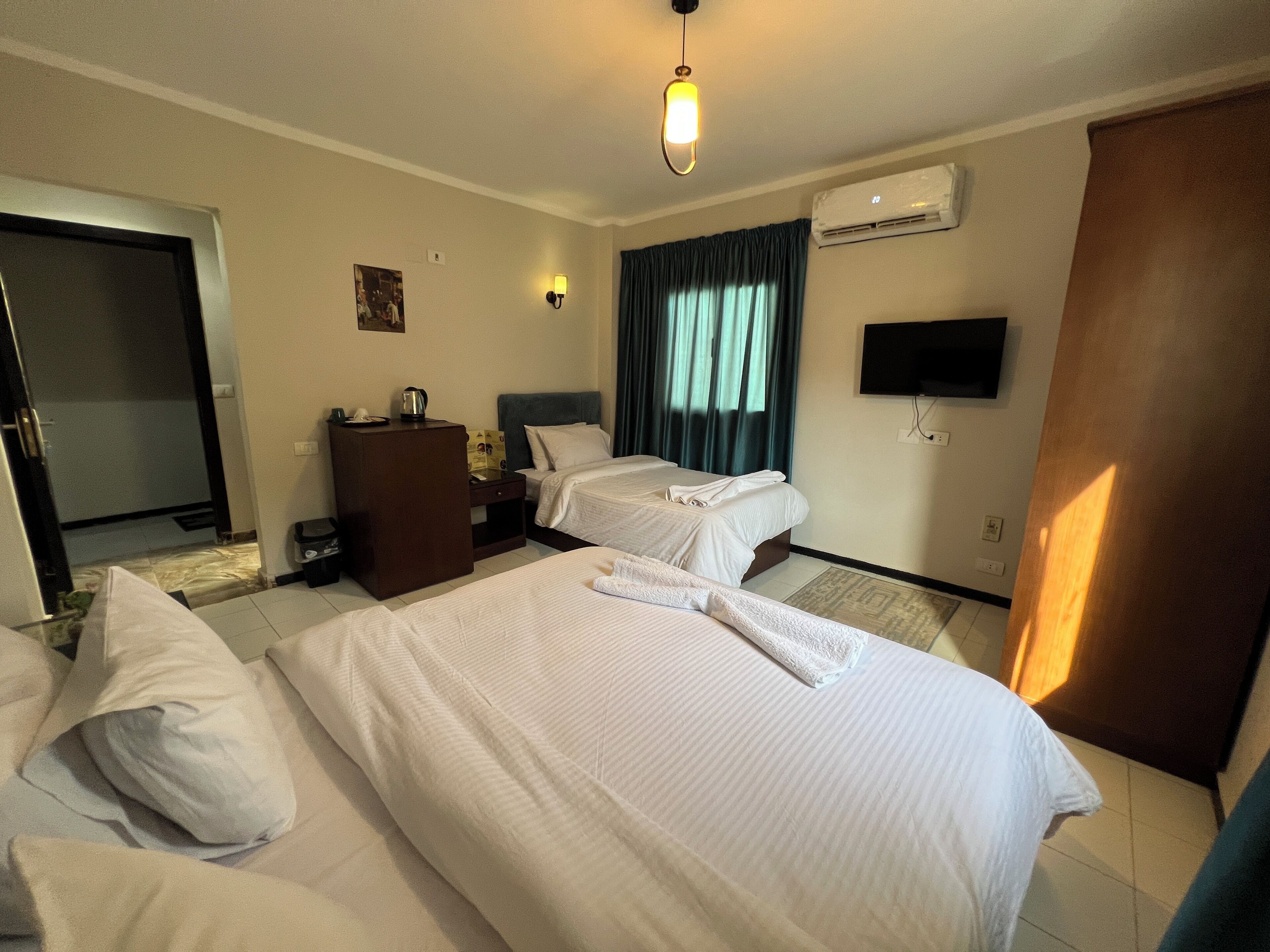 A hotel room with two beds, a desk, a chair, a television, and an air conditioning unit.