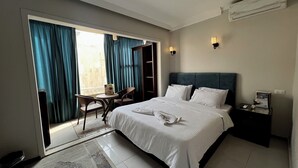 Une chambre d’hôtel avec un lit, une petite table avec des chaises, une table de chevet et une vue sur l’extérieur grâce à une grande fenêtre avec des rideaux.