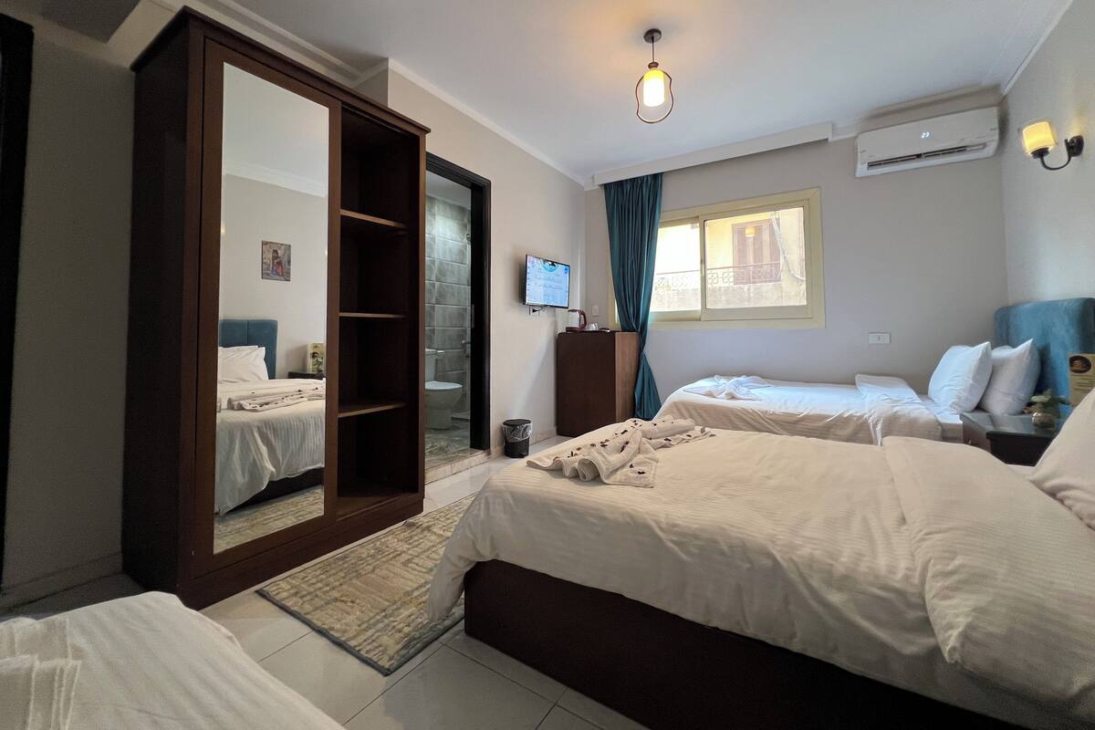 A hotel room with two beds, a wardrobe, a TV, and a window with curtains.