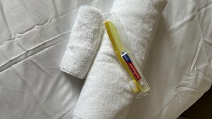 A white towel and a yellow toothbrush on a white bed.