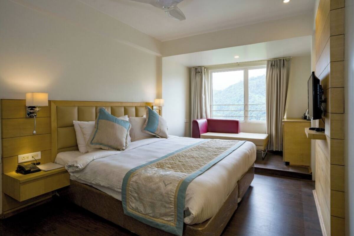 A hotel room with a large bed, bedside tables, a desk, a chair, and a window with curtains.
