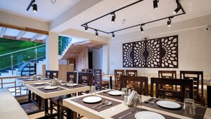A modern dining area with long tables, chairs, and a decorative wall piece. - Hotel Finger lime (Gangtok)