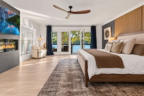 Une chambre à coucher moderne avec un grand lit, un ventilateur de plafond, une cheminée et une vue sur l’extérieur.