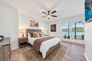 Een slaapkamer met een bed, nachtkastjes, een plafondventilator, een raam met uitzicht en een vloerkleed.