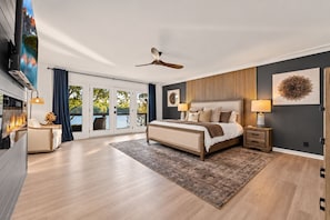 A modern bedroom with a large bed, a ceiling fan, a fireplace, and a view through the glass doors. - Lakefront ·Hot Tub ·Sauna · Private Dock ·Fire Pit (Hot Springs Village)