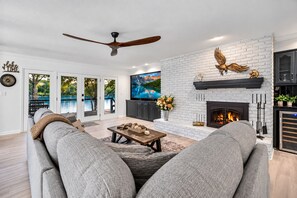 A modern living room with a fireplace, a ceiling fan, and a large TV.