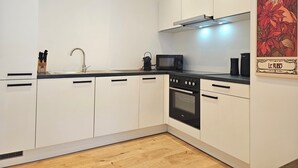 A modern kitchen with white cabinets, a black countertop, a microwave, an oven, and a sink. - Ruby - Right next to the castle, balcony, PS4 & Stream (Montabaur)