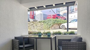 A balcony with wicker chairs and a table, overlooking a street with parked cars and a building with a red door. - Ruby - Right next to the castle, balcony, PS4 & Stream (Montabaur)