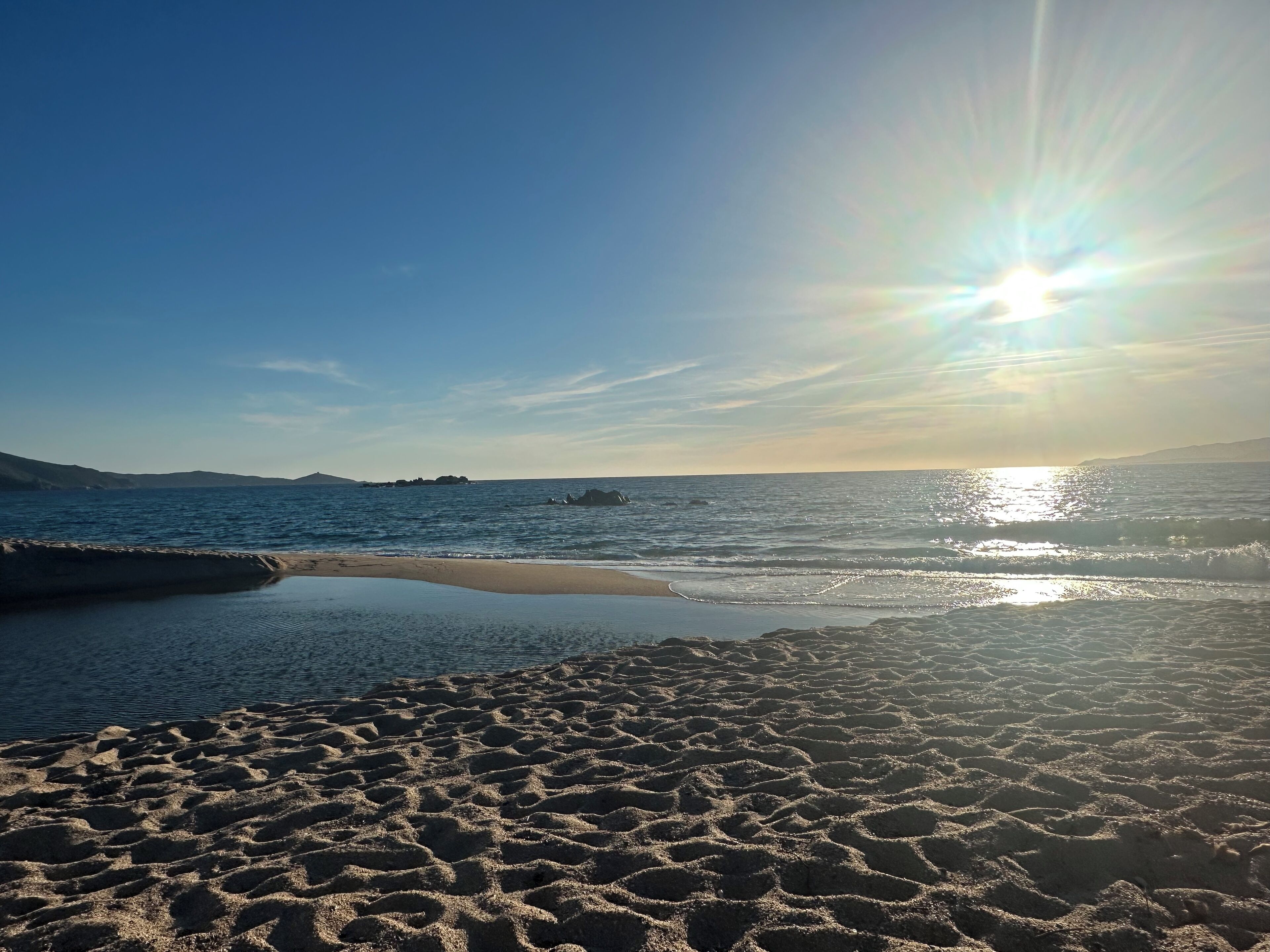 A beach with clear skies and the sun setting over the water.